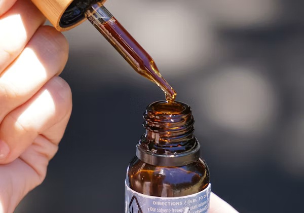Botol kaca cokelat minyak CBD dipegang di tangan